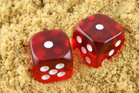 2 Dice showing snake eyes - half buried in the sand