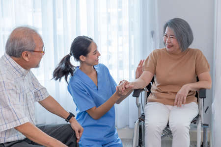 Young nurse taking care elderly disabled woman sitting in a wheelchair with copyspace. A female supporter assisting a senior patein while she is smilling.の写真素材