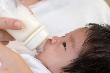 One month old baby embraced by mother and drinking milk from baby bottleの写真素材