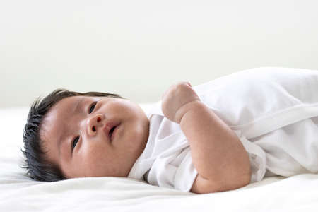 Baby lying on sheets and having a sad faceの写真素材