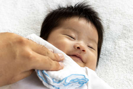 Man's hand wiping the baby's mouth with a clothの写真素材