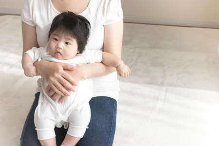 Mother in her 30s and baby sitting on her lap, 0 years old, 4 months old, girl