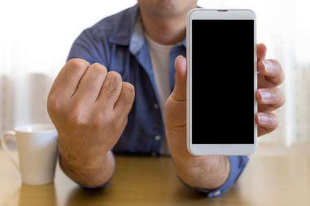 A man sitting on a chair and showing the screen of a smartphone (30s, Japanese, plain clothes)