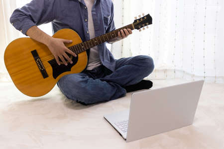 Image of a man practicing guitar while looking at a computerの写真素材