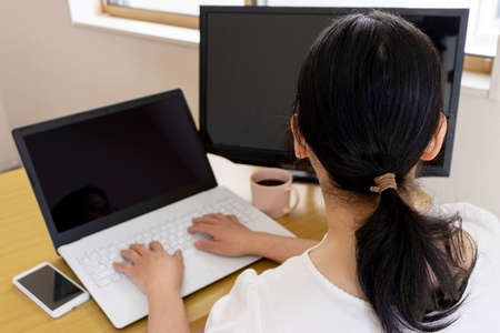Image of a woman working on a computer at a table at homeの写真素材