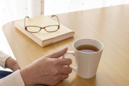 A senior woman taking a reading break. Books, tea, glassesの写真素材