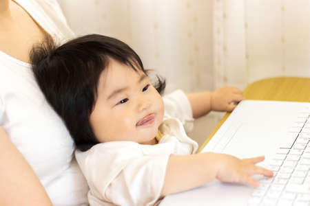 A woman who sits her baby on her lap and uses a laptop. Baby (0 years old, 8 months old, Japanese, girl)の写真素材