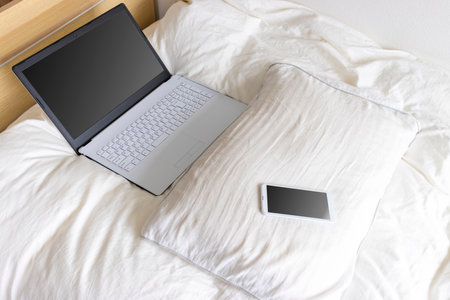 Image of using a laptop and smartphone in bedの写真素材