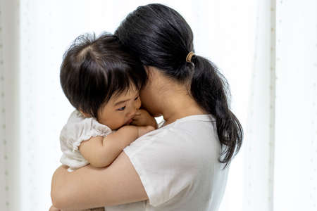 Grumpy baby hugged by mother (1 year old, girl, Japanese)
