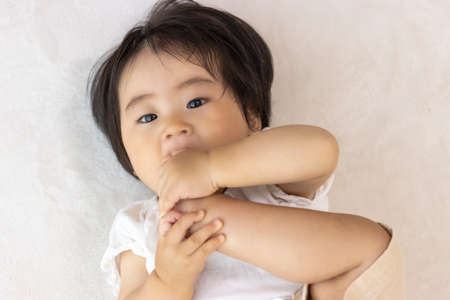 Baby lying down and licking feet (1 year old, Japanese, girl)の写真素材