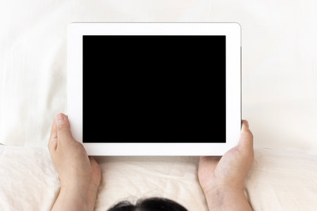Young woman (Japanese, 30s) lying on the bed and using a tablet deviceの写真素材