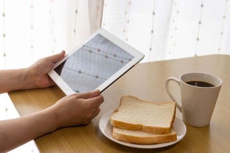 Image of a woman's hand using a tablet device while eating breakfastの写真素材