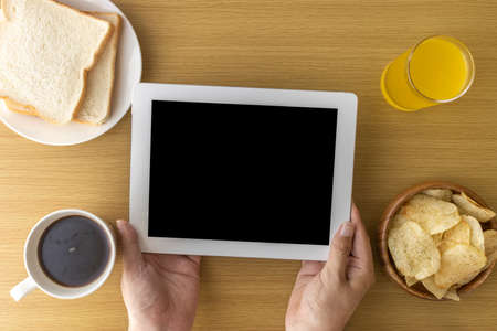 Men's hands using a tablet device while eating a light mealの写真素材