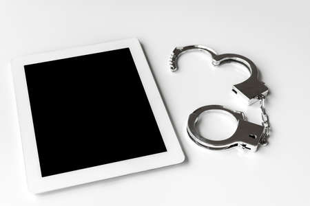 Tablet terminal and handcuffs. Image of cybercrimeの写真素材