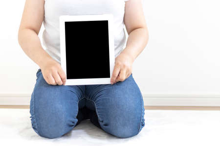Image of a woman sitting on a carpet and using a tablet device (30s, Japanese, no face)の写真素材
