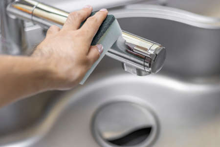 Image of a man's hand cleaning a kitchen faucet