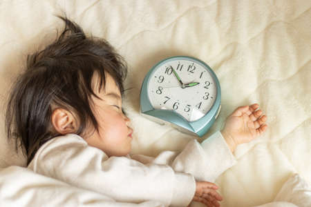 A baby taking a nap and a clock (1 year and 5 months old, Japanese, girl). Childcare time imageの写真素材