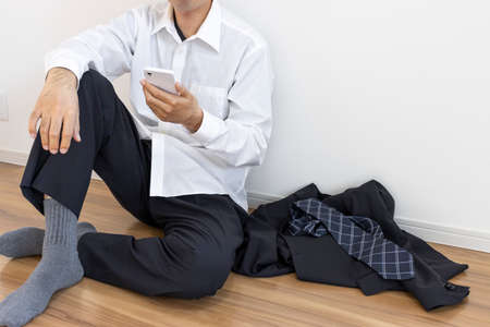 A man who takes off his suit, relaxes and uses a smartphoneの写真素材