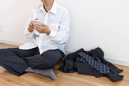 A man who takes off his suit, relaxes and uses a smartphoneの写真素材