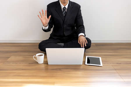 A man in a suit sitting on the floor and making a video call on his laptopの写真素材