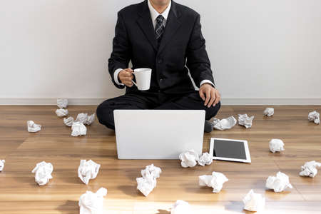 A man in a suit sitting on the floor and operating a laptop and a lot of rolled paperの写真素材