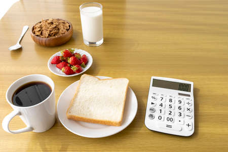 Calculator and breakfast (bread, flakes, strawberries, coffee, milk). Image of food expensesの写真素材