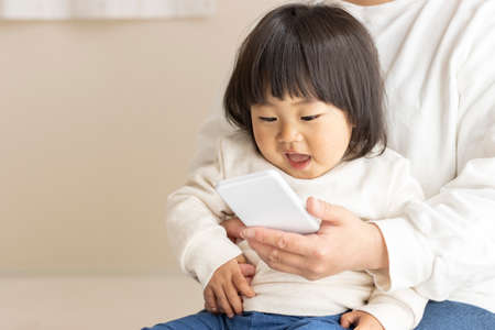 A baby looking at a smartphone (1 year and 8 months old, girl, Japanese) and a mother's hand showing it (30s, Japanese)の写真素材