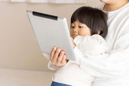 A baby (1 year and 8 months old, girl, Japanese) looking at a tablet device and a mother's hand (30s, Japanese) showing itの写真素材