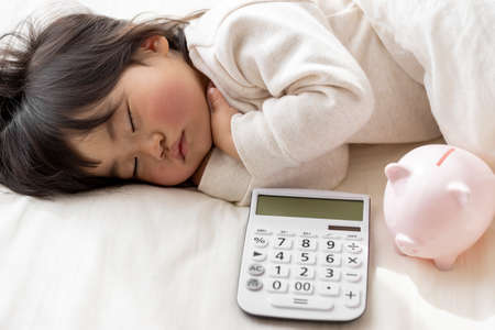 A baby taking a nap, a calculator and a piggy bank (1 year and 8 months old, Japanese, girl). Childcare cost imageの写真素材