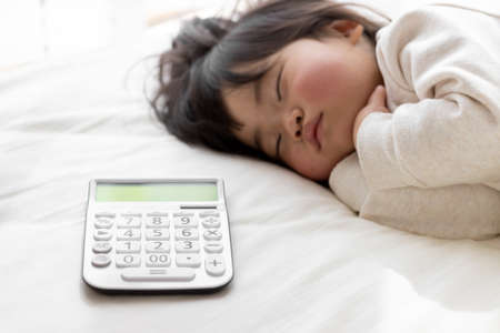 A baby taking a nap and a calculator (1 year and 8 months old, Japanese, girl). Childcare cost imageの写真素材