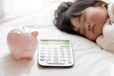 A baby taking a nap, a calculator and a piggy bank (1 year and 8 months old, Japanese, girl). Childcare cost imageの写真素材