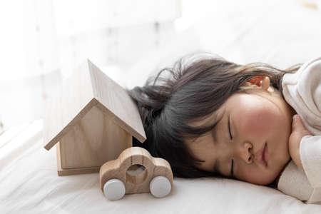 A baby taking a nap, a toy house and a car (1 year and 8 months old, Japanese, girl). Image of life planning with childrenの写真素材