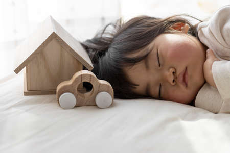 A baby taking a nap, a toy house and a car (1 year and 8 months old, Japanese, girl). Image of life planning with childrenの写真素材