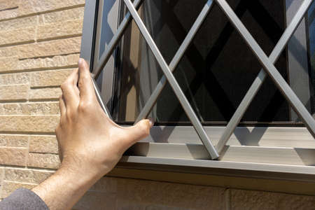 A man's hand checking the grid of a windowの写真素材