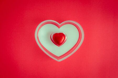 Top view of heart shaped candy in a box placed on a red background. Red heart in a jar on a red...