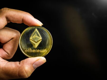 Hand is holding gold ethereum coin on a black screen. Business value cryptocurrency are expensive.