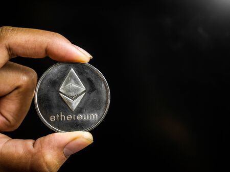 Hand is holding silver ethereum coin on a black screen. Business value cryptocurrency are expensive.