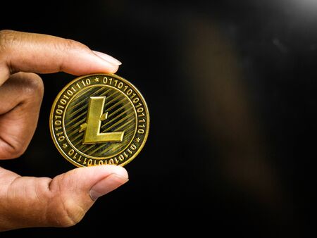 Hand is holding gold litecoin on a black screen. Business value cryptocurrency are expensive.