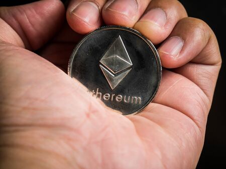 Business male hand is holding silver ethereum coin. Business value cryptocurrency are expensive.