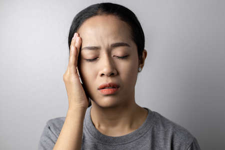 Young woman with of stress and headaches on a gray background. Asian woman with a headache. Women...
