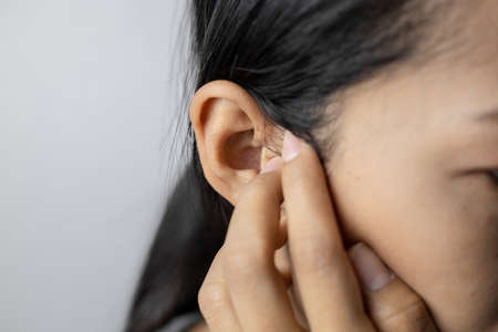 Young woman with of earache on a gray background. Asian  woman is suffering of earache. Women with a...