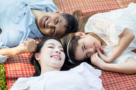 Parents and children at the squat and smiling on the mat in the park. Asian family lying on a mat in...