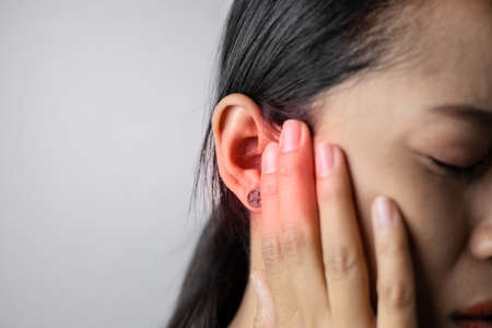 Young woman with of earache on a gray background. Asian  woman is suffering of earache. Women with a lot of ear pain.の写真素材