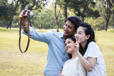 Asian families are taking family photos in a public garden for souvenirs. Parents and children take pictures together in the parkの写真素材