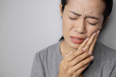 Woman put her hand on her cheek due to toothache. Asian  woman is suffering of toothache. Young woman with of toothache on a gray background.の写真素材