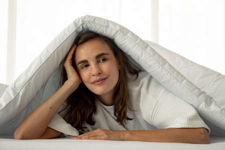 Beautiful woman under a white blanket and smile on the bed in the bedroom. Concept relax in the...