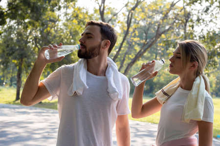 Young couples who drink water after exercising in the park in the morning. Concept couples exercise...