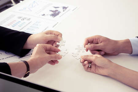 Hand holding the puzzles for the businessmen to work together as a team. Concept of planning work as a teamwork. Closeup of businesspeople holding jigsaw puzzle.の写真素材