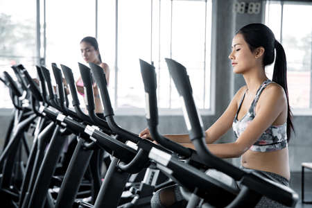 Asian young women are exercising with the cardio on the exercise machine in the gym with smile....