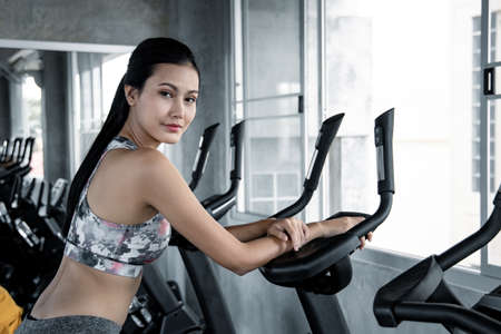 Asian young women are exercising with the cardio on the exercise machine in the gym with smile....